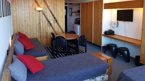 Un espacio habitable compacto con sofá, una mesa de comedor con sillas, una zona de cocina y un televisor montado.