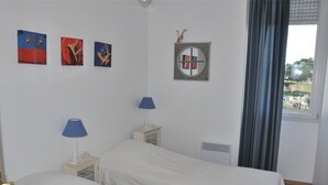 A room with two beds, a window with curtains, and three wall-mounted pictures. - 2-bedroom sea view apartment in Trégastel with parking (Trégastel)