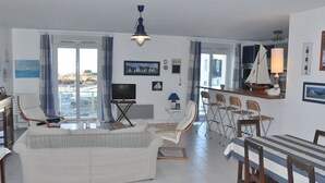 A spacious living area with a sofa, chairs, a dining table, and a TV. - 2-bedroom sea view apartment in Trégastel with parking (Trégastel)