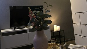 Een moderne woonkamer met een flatscreen televisie, een roze vaas met bloemen, kaarsen en een tijdschrift op een dienblad.