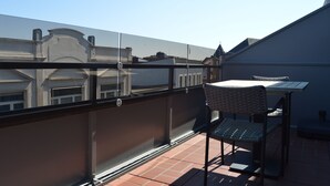 Een balkon met een glazen hekwerk, een rieten stoel en een klein tafeltje.