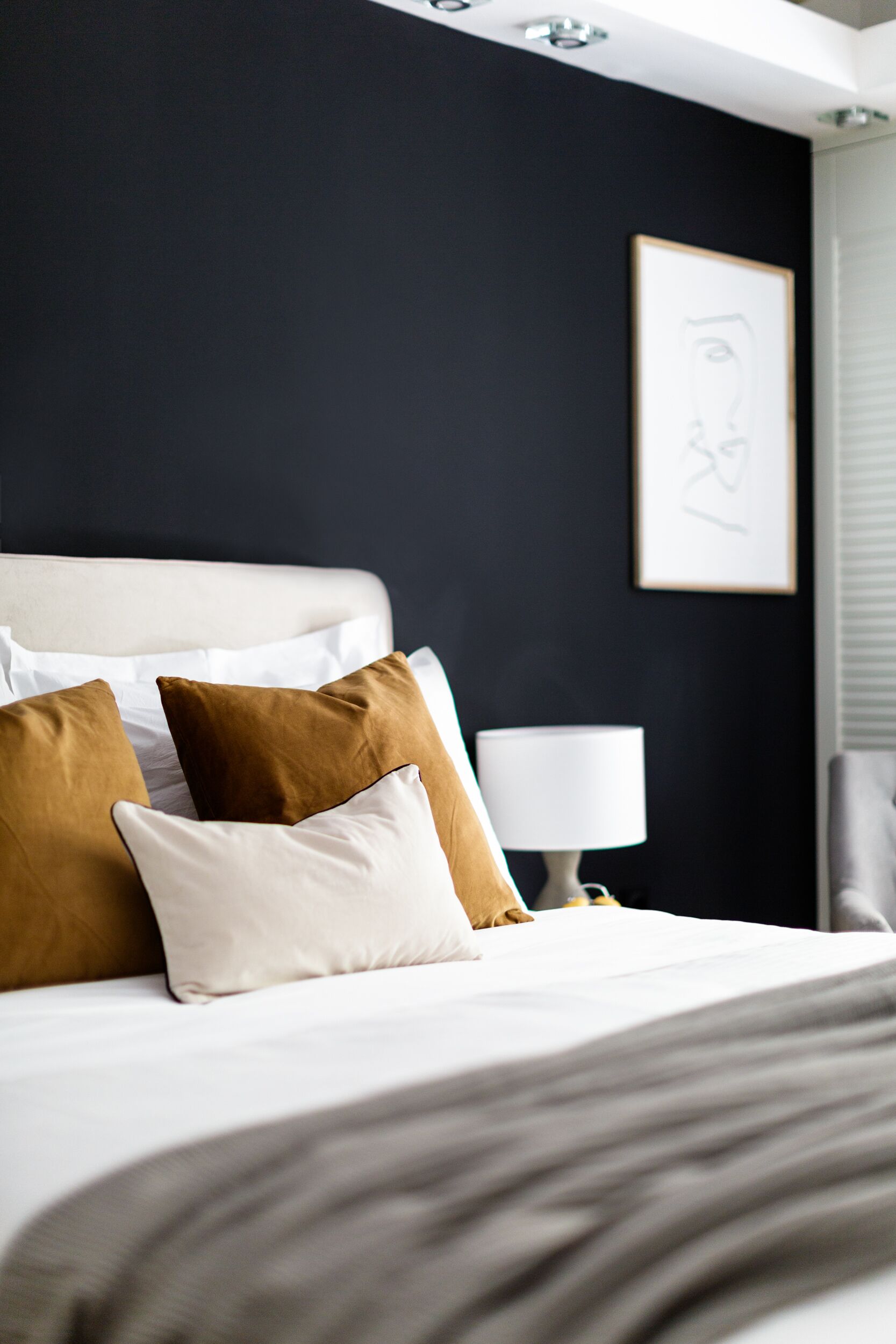 A neatly made bed with white and brown pillows, a bedside lamp, and a framed artwork on the wall.