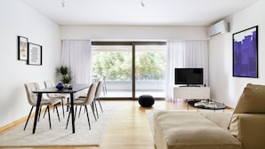 A modern living room with a sofa, a dining table with chairs, a TV, and a large window with curtains. - UPSTREET Modern 1BD Apt Acropolis Museum (Athens)