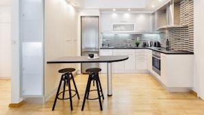 A modern kitchen with white cabinetry, a black countertop, and two stools. - UPSTREET Modern 1BD Apt Acropolis Museum (Athens)