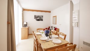 Un coin repas avec une table en bois dressée pour quatre personnes, des chaises, un petit meuble, un miroir et un tableau accroché au mur.