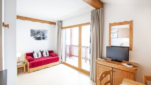 A room with a wooden ceiling, a red sofa with patterned cushions, a television on a wooden cabinet, and a sliding glass door leading to an outdoor area.