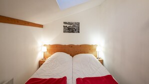 Ein Schlafzimmer mit Holz-Kopfteil, zwei Nachttischlampen, einem Bett mit weißer und roter Bettwäsche, einem kleinen Schwarz-Weiß-Foto an der Wand und einem Oberlicht.