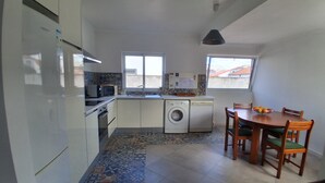 A compact kitchen with a washing machine, a microwave, and a sink. There is a dining table with chairs and a window providing natural light. - AL at Quinta do Navio (Capelas)