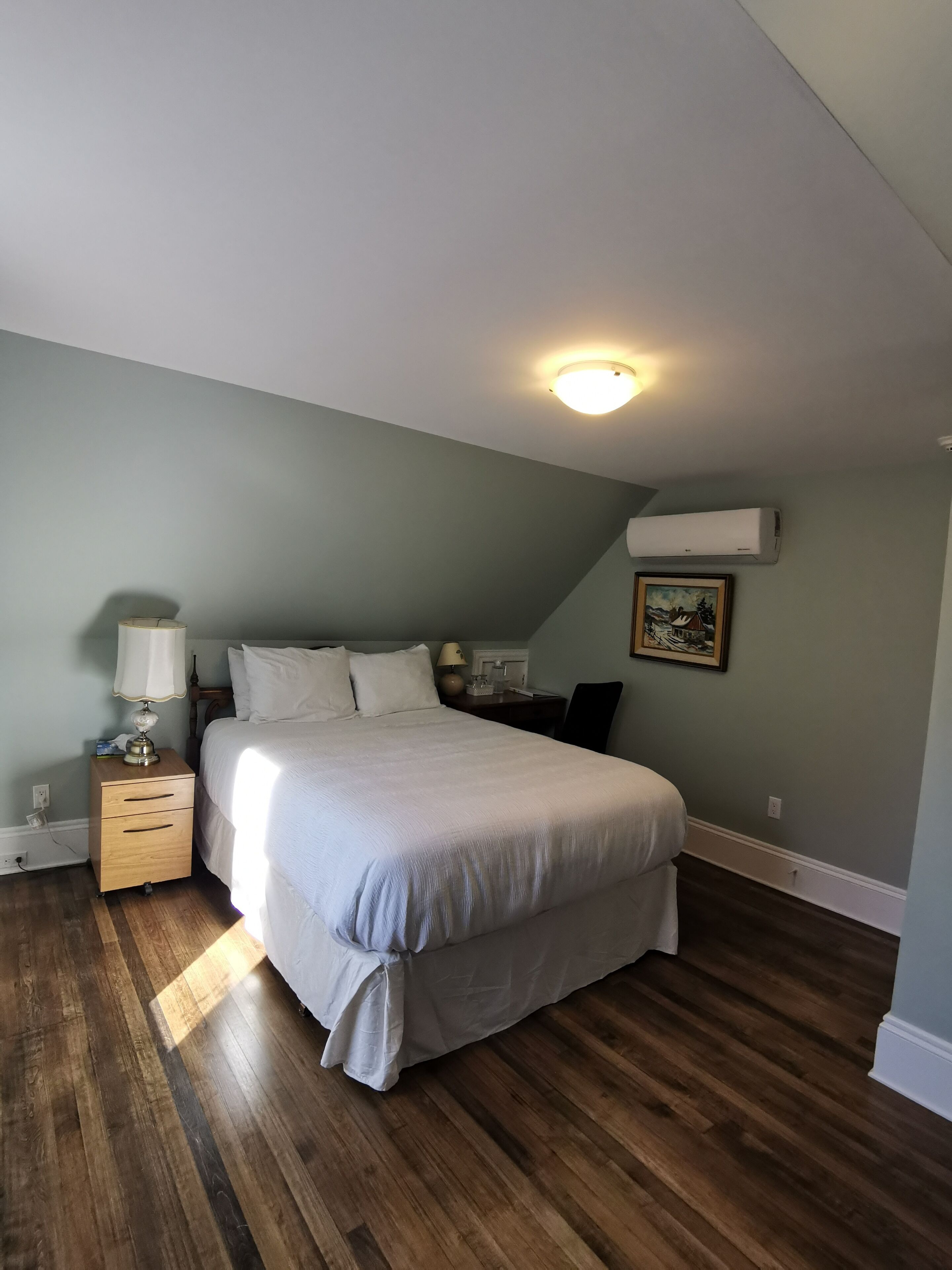 A bedroom with a bed, nightstand, lamp, and a painting on the wall.