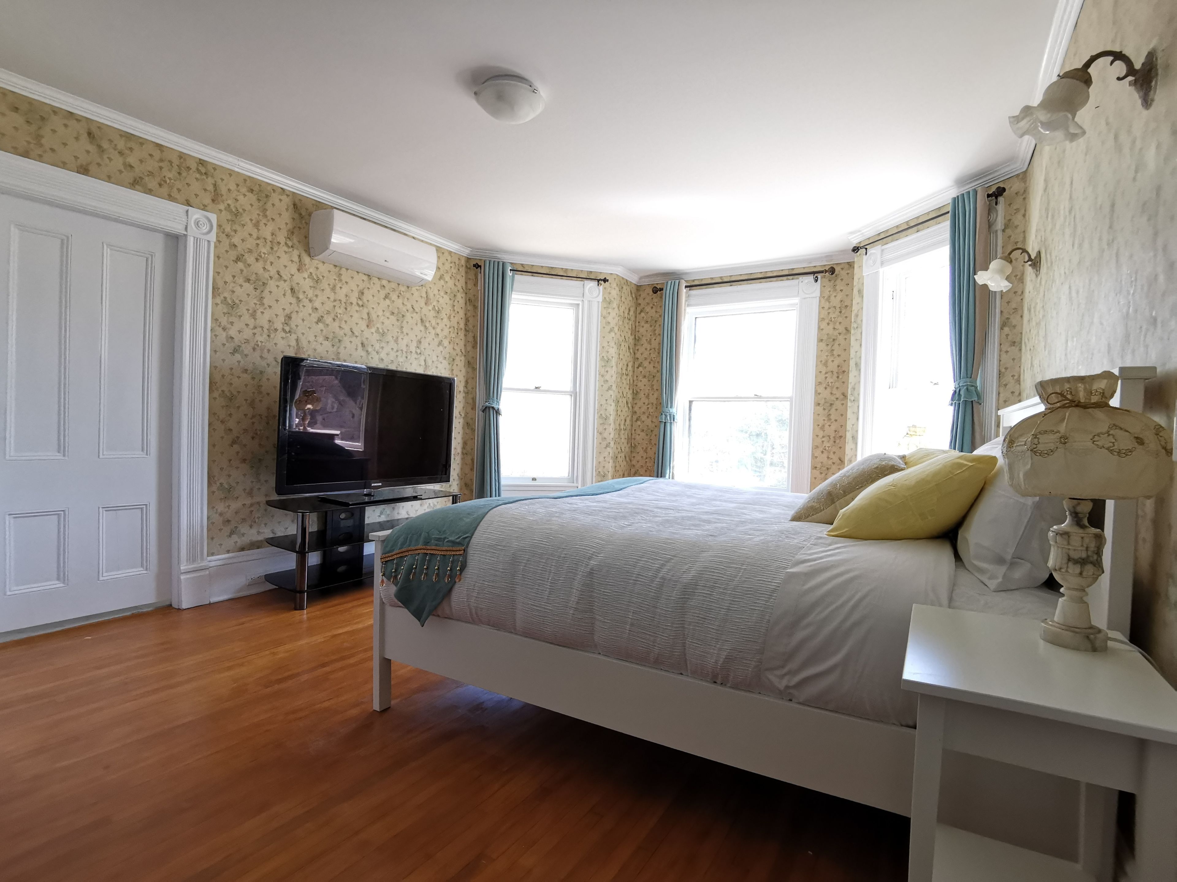 A bedroom with a bed, a television, a lamp, and a window with curtains.
