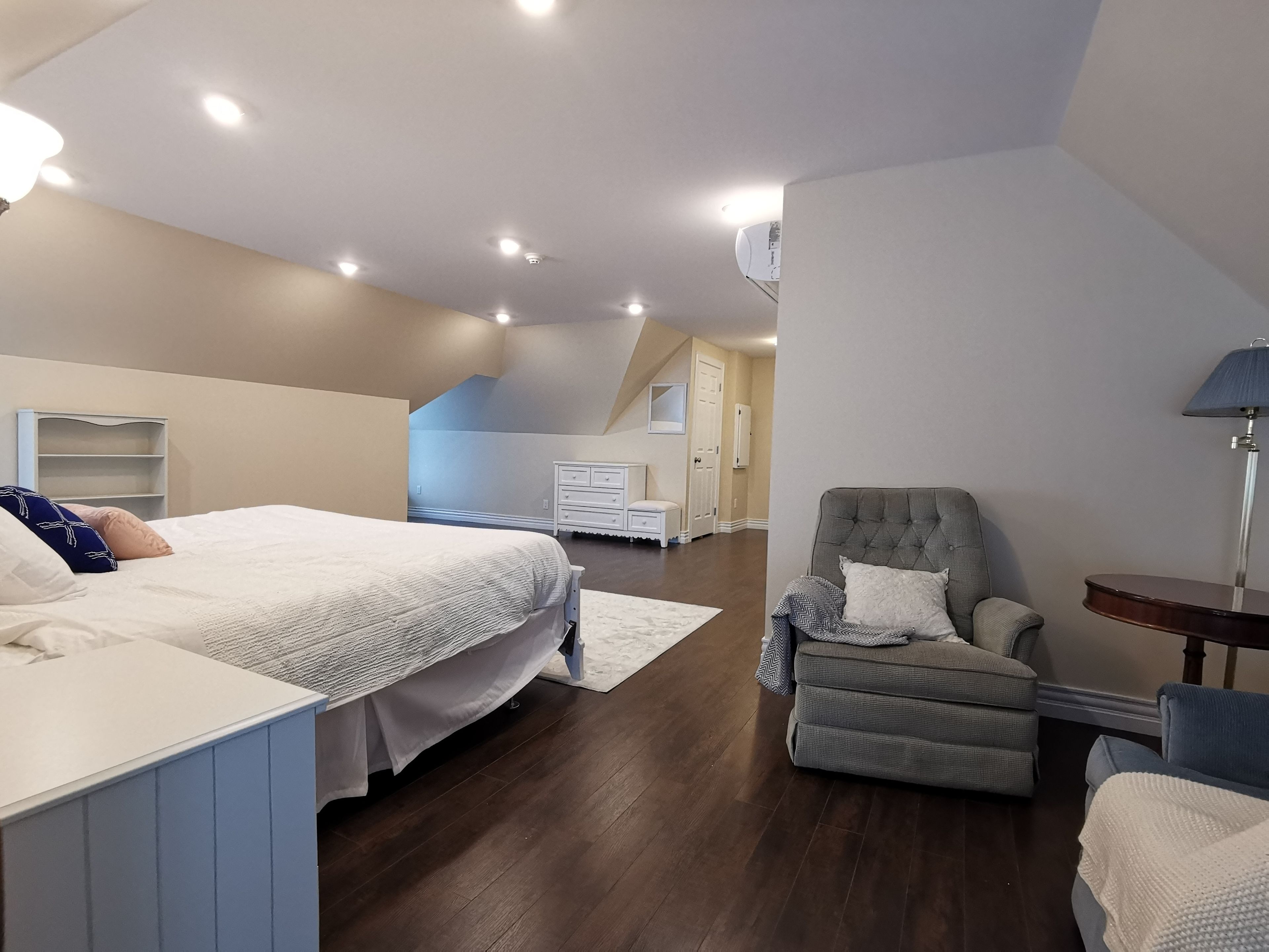 Un dormitorio con cama, una silla, un escritorio y una lámpara.