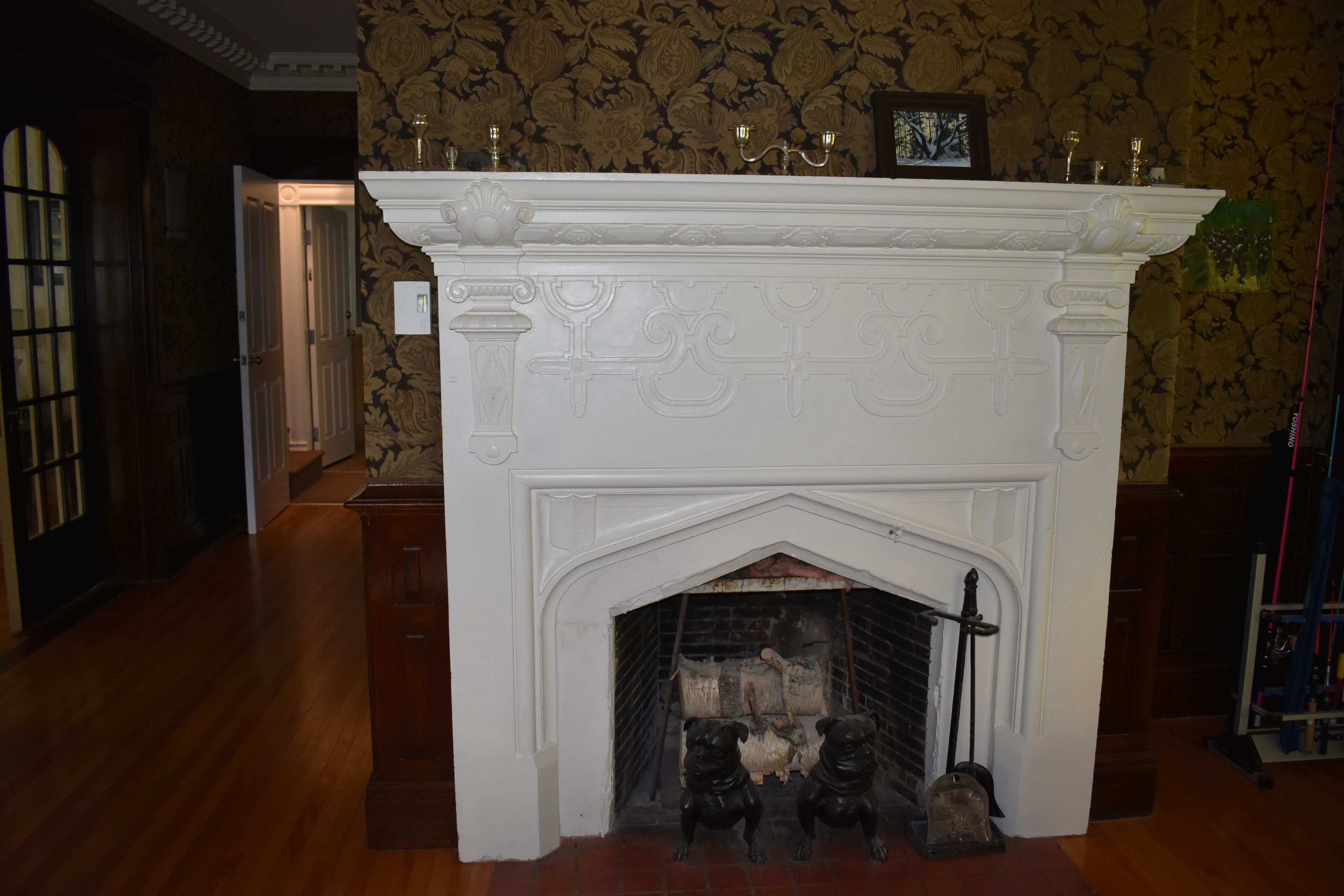 A fireplace with a white mantel and decorative carvings, flanked by two black dog statues.