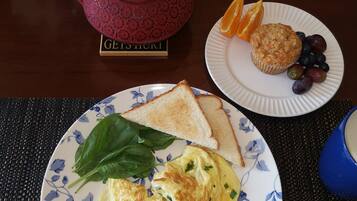 A breakfast setting with toast, spinach, scrambled eggs, a muffin, and fruit on plates, a teapot, and salt and pepper shakers on a table.