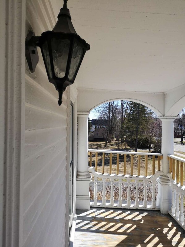 A covered porch with white columns and a wooden railing. - By The River Bed&breakfast (Fredericton)