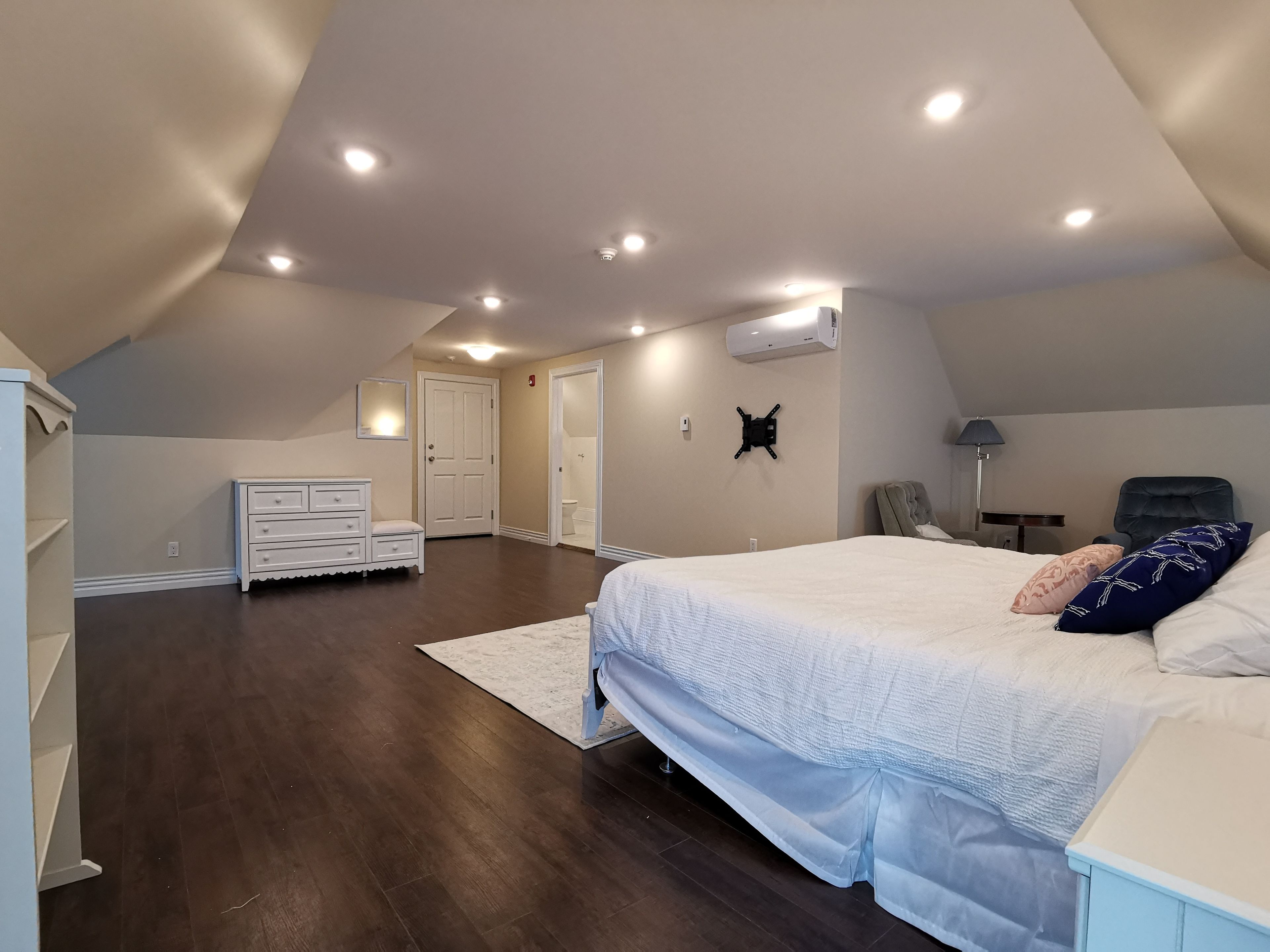A bedroom with a large bed, a dresser, a chair, and a desk with a lamp.