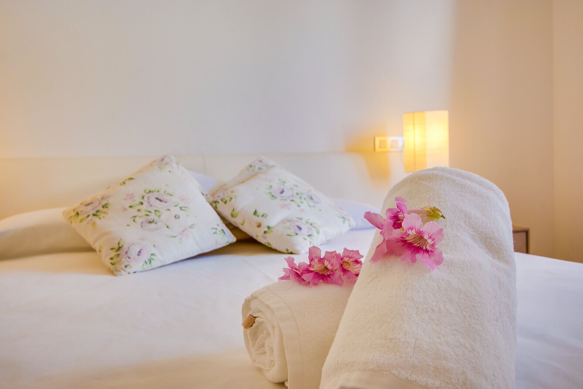 Een net opgemaakt bed met bloemenkussens en een handdoek met bloemendesign.