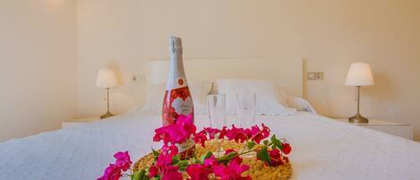 Een keurig opgemaakt bed met een fles champagne, een geweven mand met bloemen en twee bedlampjes in een hotelkamer.