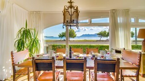 A dining area with a table set for six, a chandelier, and a view of a body of water and mountains. - House Puerto Pollensa Llenaire with pool (Puerto Pollensa)