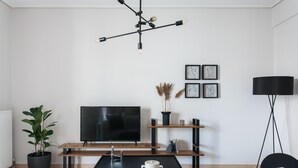 Un salon moderne avec un téléviseur à écran plat, une table basse noire, une plante en pot, un banc en bois et un lampadaire noir.