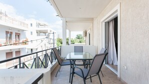 Un balcon avec une table et des chaises en verre, donnant sur un quartier résidentiel.