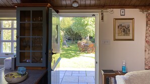 Een kamer met een houten plafond, een deur naar een buitenruimte met een gazon en een tafel, en een boekenkast met boeken en een fles handdesinfectiemiddel.