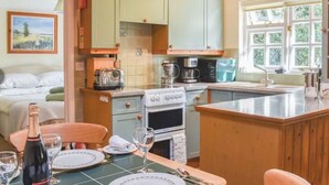 A cozy kitchen with a dining area, wooden cabinets, a stove, and a window with a view of greenery. - Stable Conversion Near Lulworth Cove/Jurassic Coast (Dorchester)