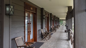 Un couloir couvert, agrémenté de chaises et de tables en bois, de portes en bois dotées de panneaux de verre et de lanternes fixées aux murs.