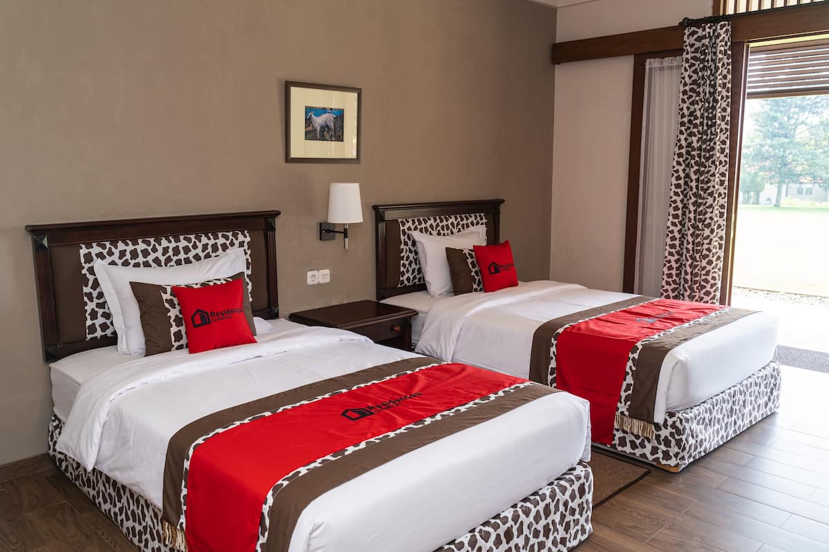 Een hotelkamer met twee bedden, elk met een gestreept hoofdeinde, een rood-witte sprei en een kussen met het logo van het hotel.