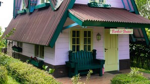 Une maison avec un toit triangulaire distinctif, un porche à l’avant avec un banc et une enseigne sur laquelle on peut lire « Maison de Barbie ».
