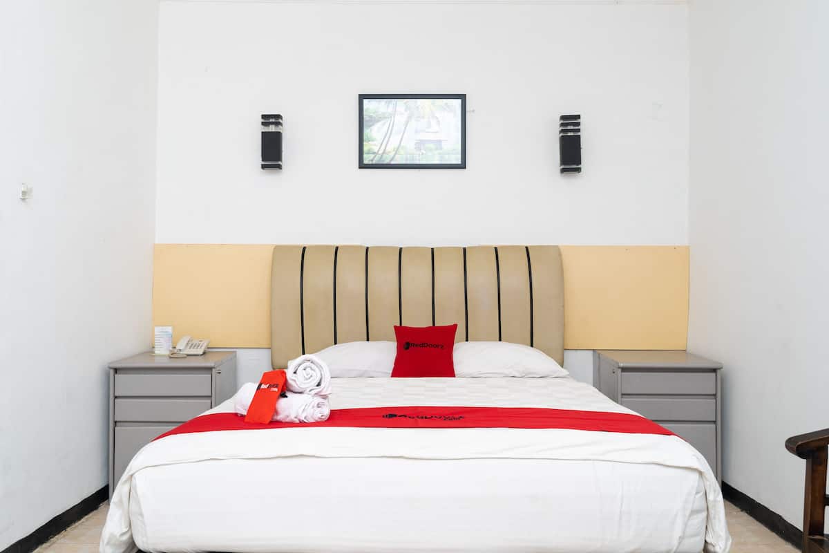 Een hotelkamer met een bed, twee nachtkastjes, een telefoon, een rood kussen, een rode plaid en een lijstje op de muur.