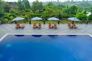 A swimming pool with lounge chairs and umbrellas, surrounded by a tiled deck and lush greenery.