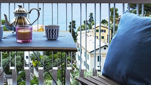 Ein Balkon mit Tisch, Teekanne, Kerze und Blick auf das Meer und Gebäude.