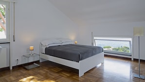 Ein modernes Schlafzimmer mit Bett, Nachttischen, einer Lampe und Blick aufs Meer.