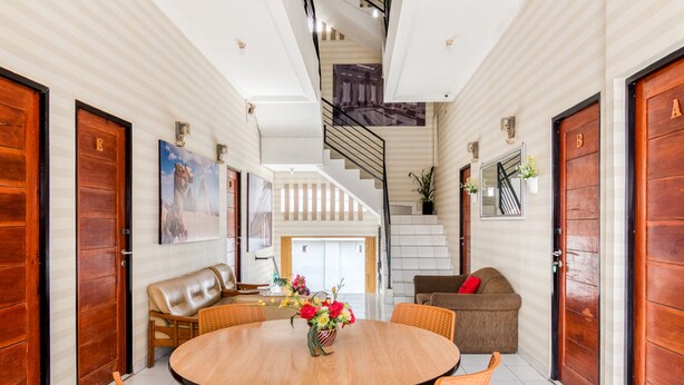 A spacious living area with a round wooden table, orange wicker chairs, a leather sofa, and a staircase leading to an upper floor. - RedDoorz Plus near Hayam Wuruk 2 (Jakarta)