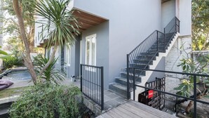 Un bâtiment moderne doté d’une terrasse en bois, d’un escalier et d’un petit jardin agrémenté de plantes et d’un élément décoratif aquatique.