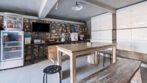 Une cuisine avec un mur en pierre, une table en bois, un réfrigérateur et un distributeur d’eau.