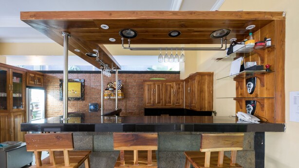 A kitchen with a wooden bar area, stools, and a brick backsplash. - RedDoorz @ Kerta Dalem Sidakarya (Denpasar)