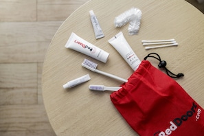 A round wooden table with a red drawstring bag, two toothbrushes, toothpaste tubes, and cotton swabs.