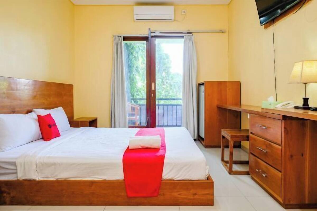 Een hotelkamer met een bed, een bureau, een stoel, een televisie en een airconditioning.