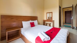 A hotel room with a wooden headboard, a white bed with a red pillow, a wooden nightstand, and a red and white checkered bedspread. - RedDoorz @ Kerta Dalem Sidakarya (Denpasar)