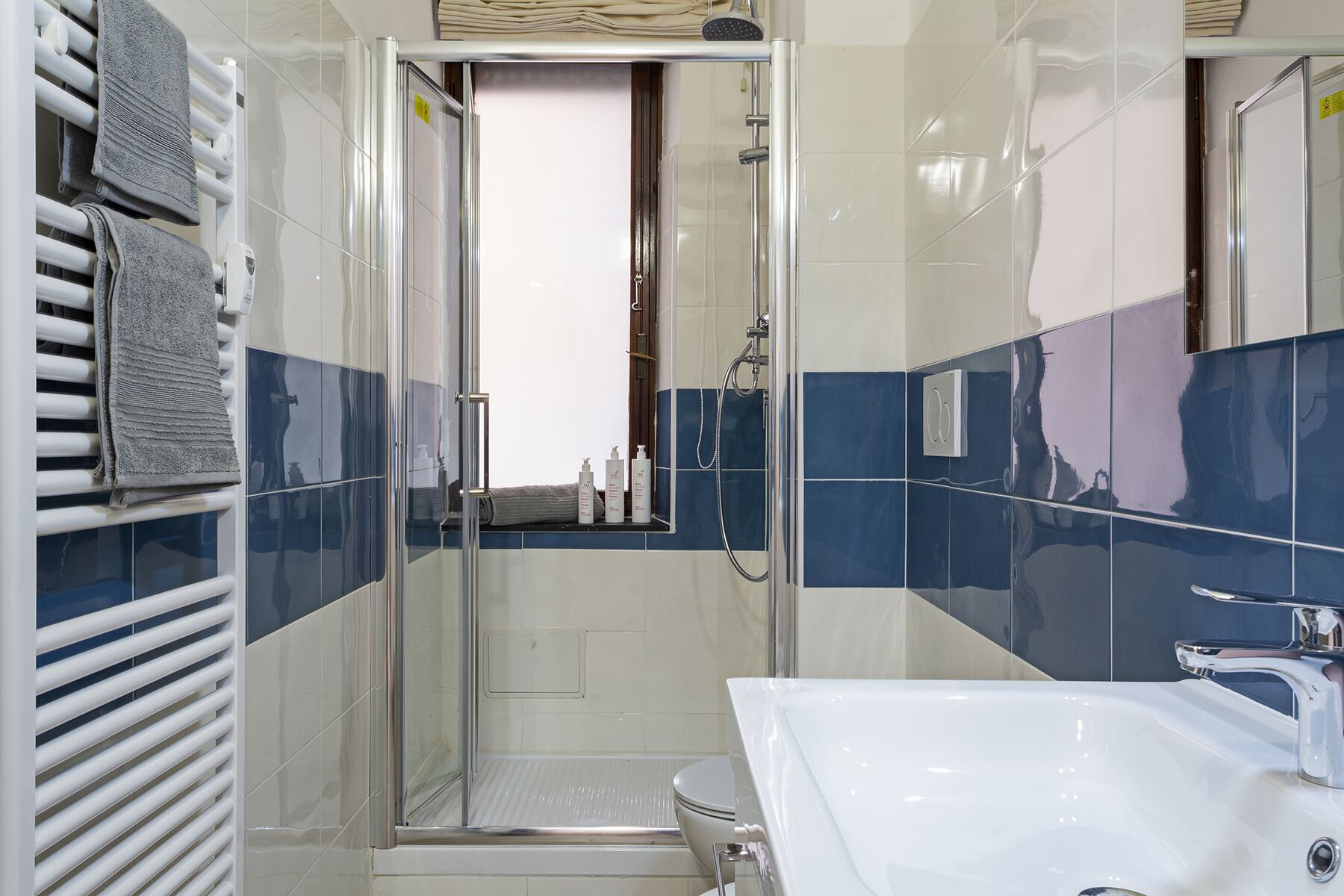 Une salle de bain moderne avec une douche à parois de verre, un lavabo blanc et des murs recouverts de carreaux bleus.