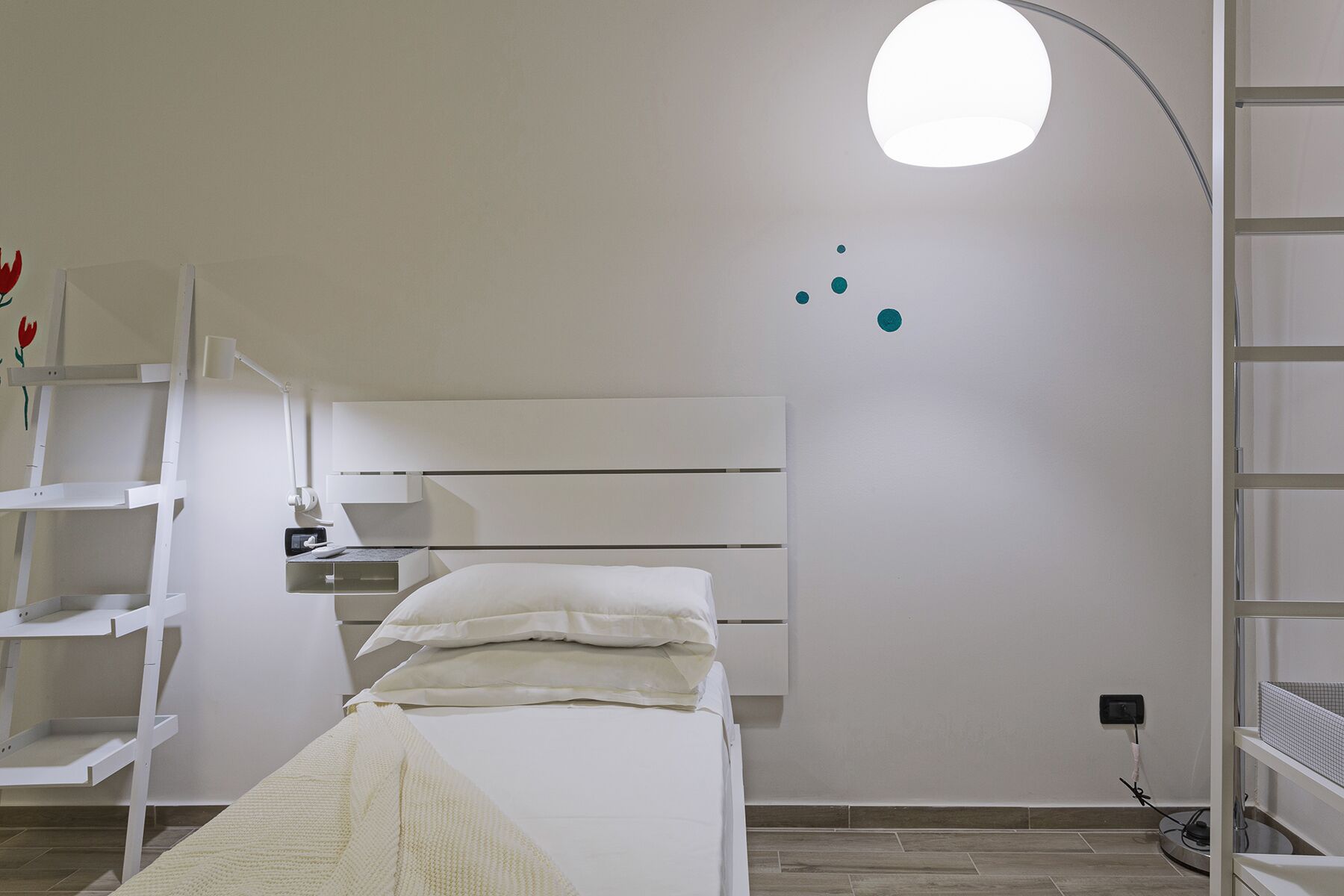 A minimalist bedroom with a bed, a bedside lamp, and a wall-mounted shelf.