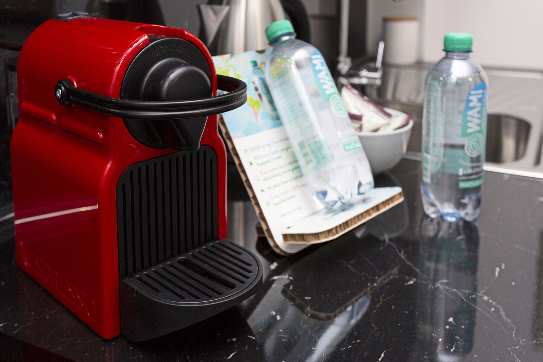 Eine rote Espressomaschine auf einer Küchenarbeitsplatte, zusammen mit einer Speisekarte und zwei Wasserflaschen.
