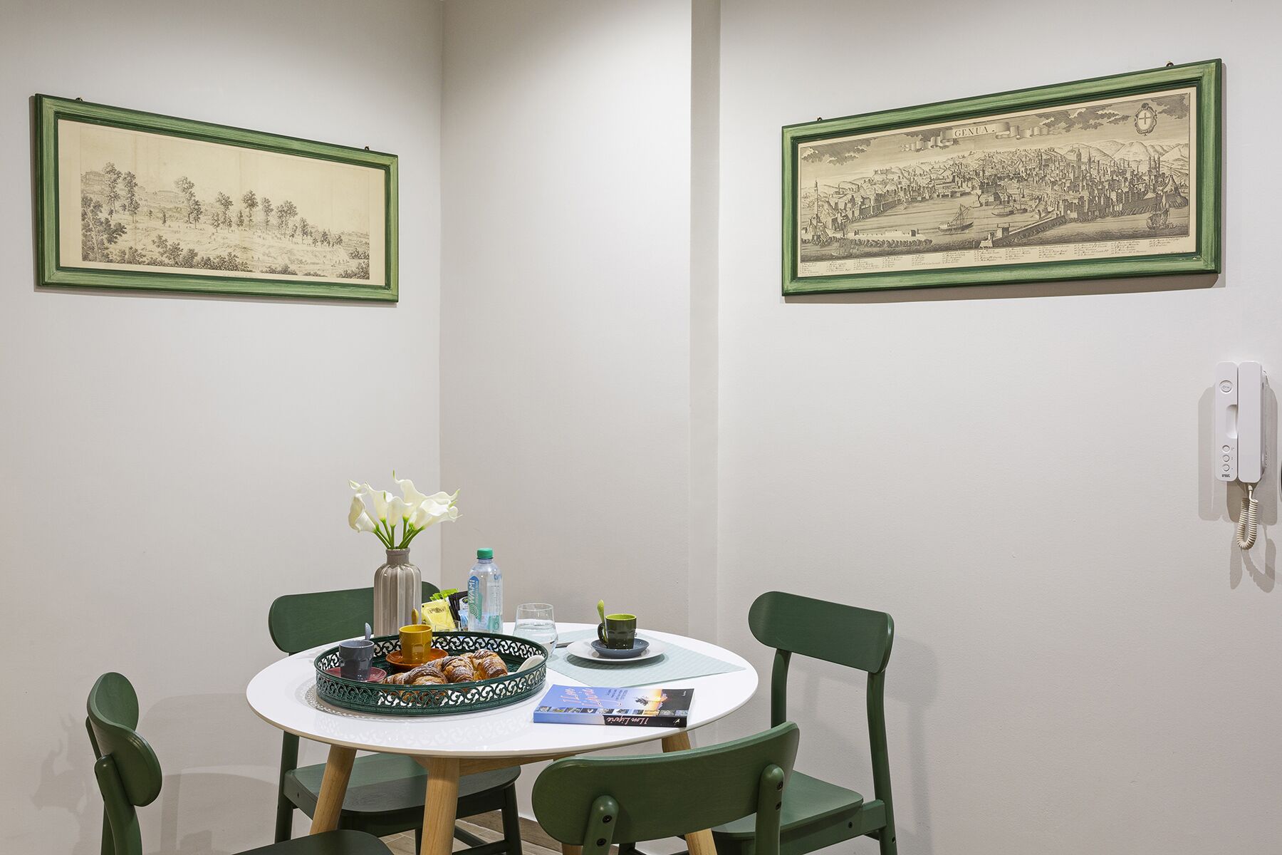 Un coin repas avec une table ronde, des chaises, un vase de fleurs et deux tableaux historiques encadrés accrochés aux murs.