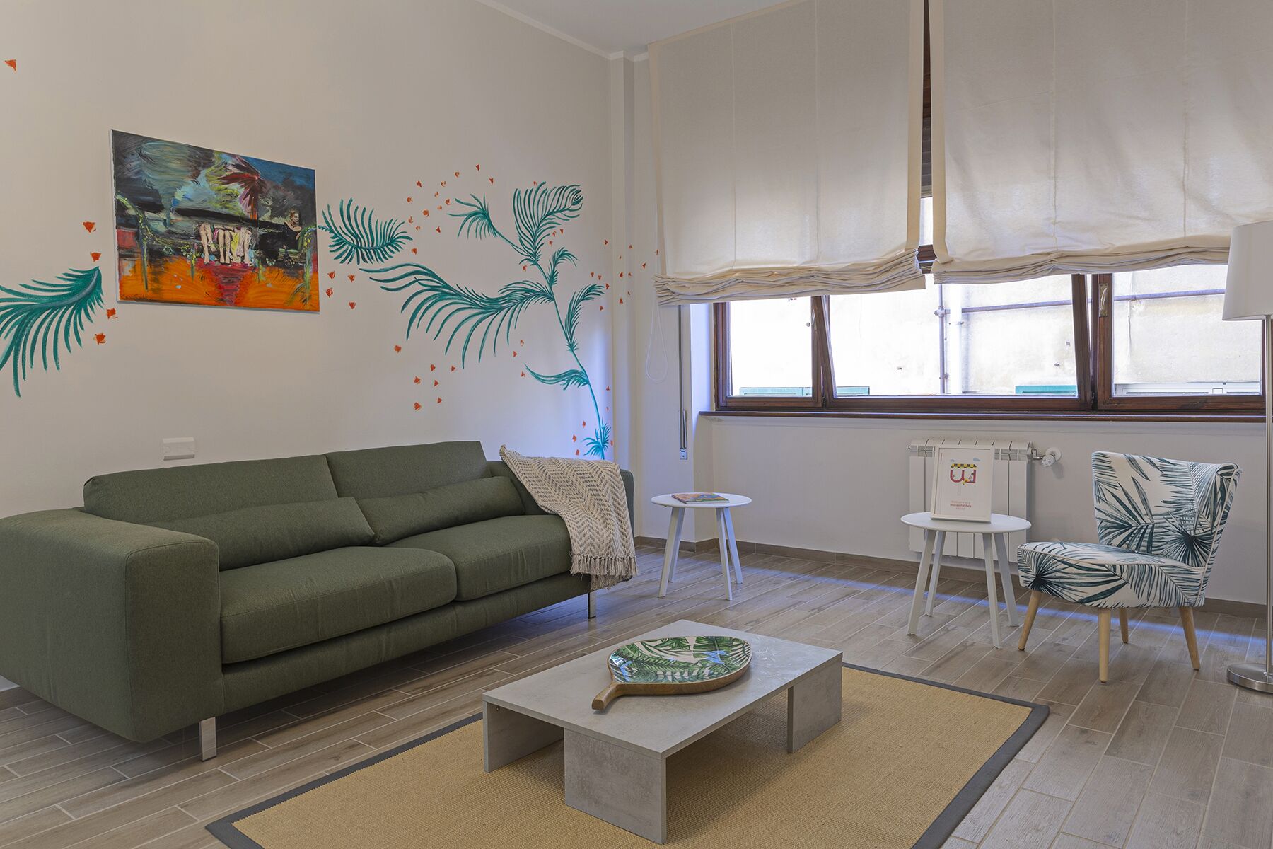A living room with a green sofa, a coffee table, a chair with a tropical print, and a painting on the wall.