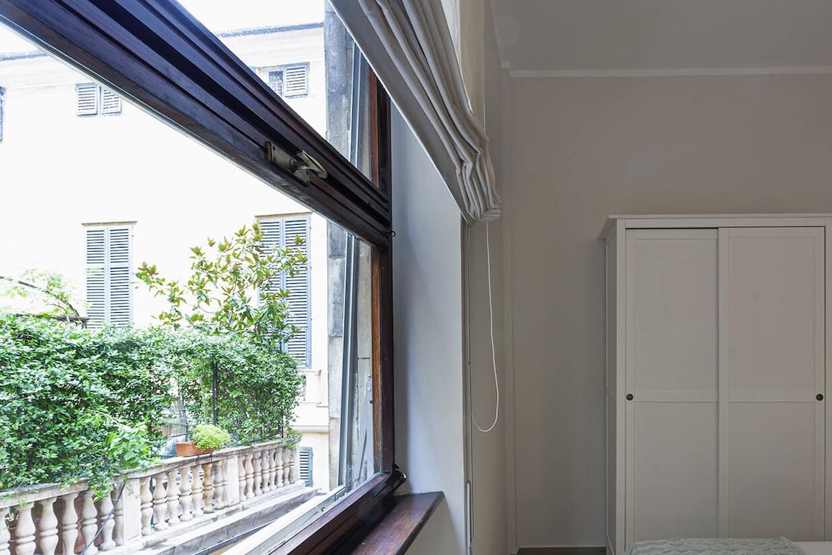 Een kamer met een balkon, een witte garderobe en een nachtkastje met een lamp.