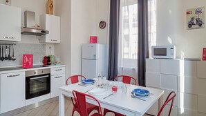 Uma cozinha moderna com armários brancos, forno embutido e área de jantar com mesa branca e cadeiras vermelhas.