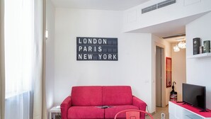 Uma sala de estar moderna com um sofá vermelho, uma mesa de jantar com copos e talheres, e um letreiro na parede listando Londres, Paris e Nova York.