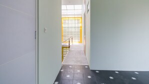 A narrow hallway with a tiled floor featuring star patterns, leading to a bright room with a window and a door with blinds. - RedDoorz near UMY Yogyakarta 3 (Sleman)