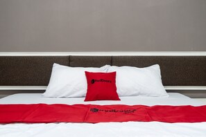 Una cama con ropa de cama blanca y una manta roja.